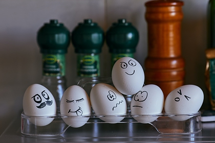 white egs with faces drawn on displaying different emotions and supporting another egg, on a glass rack