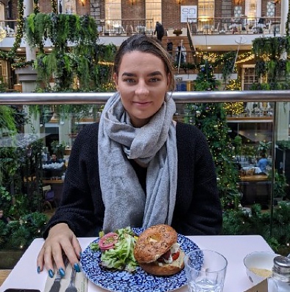 Photo of Alice wearing a grey scarf sat at a table with a meal in front of her