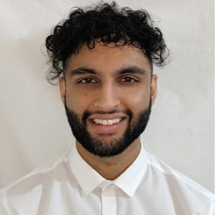 A headshot of Ameen in a white shirt against a light background. He has a beard and curly brown hair and is smiling.