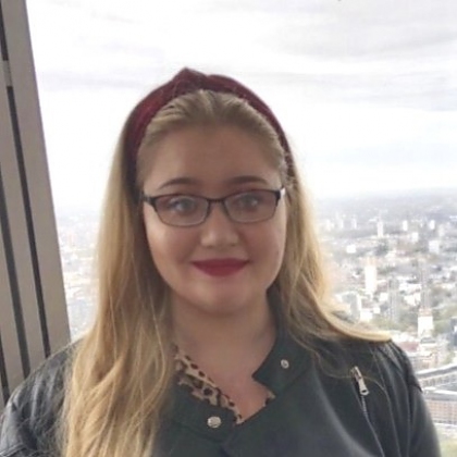 A photo of Hanna, who has long blonde hair, glasses and a red headband, wearing a leather jacket.