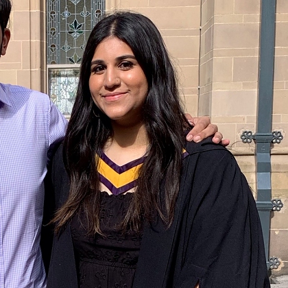 A photo of Zara who has long dark hair and is wearing her graduation gown.